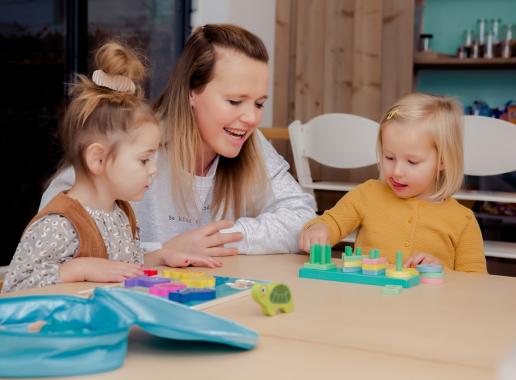 pedagogisch medewerker en twee meisje spelen aan tafel 