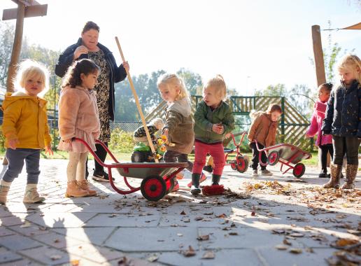 kinderen en pedagogisch medewerker vegen bladeren op