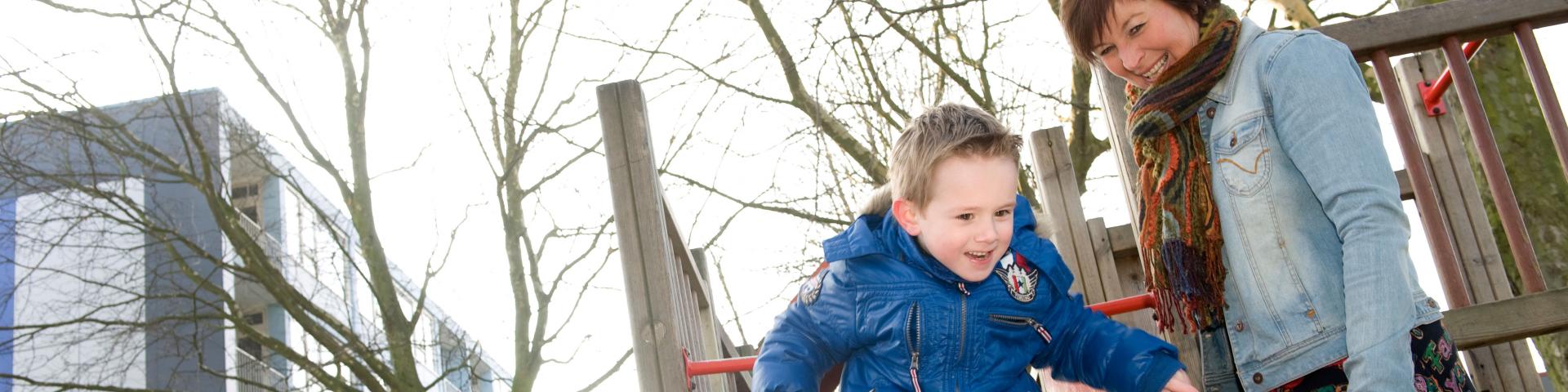 Jongentje op glijbaan en pedagogisch medewerker staat erbij