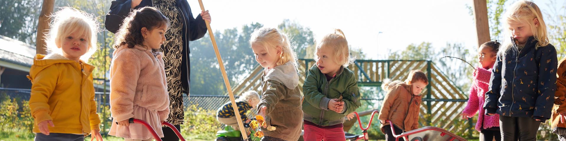 kinderen en pedagogisch medewerker vegen bladeren op  