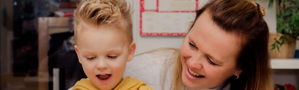 Decoratieve foto van een coach Gezonde Kinderopvang die een kind helpt. Ze lachen vrolijk.