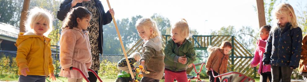 kinderen en pedagogisch medewerker vegen bladeren op  