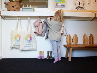 meisje hangt jas aan kaptok kinderopvang