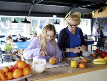 Decoratieve foto van een coach Gezonde Kinderopvang die samen met een kind fruit aan het snijden is