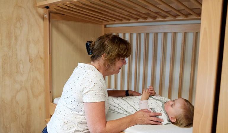 Decoratieve foto van een pedagogisch medewerker die een baby op bed legt
