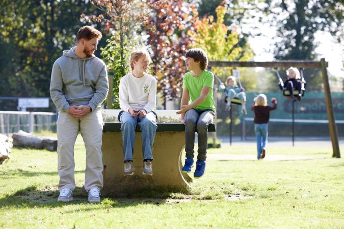 Volwassen praat buiten met kinderen zittend op een tafeltennistafel