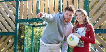 Decoratieve foto van een coach Gezonde Kinderopvang. Hij wijst een kind met een bal een richting op.