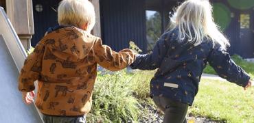 Decoratieve foto van twee kinderen. Ze lopen en hebben elkaars hand vast.