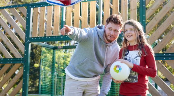 Decoratieve foto van een coach Gezonde Kinderopvang. Hij wijst een kind met een bal een richting op.