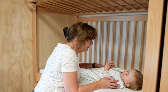Decoratieve foto van een pedagogisch medewerker die een baby op bed legt