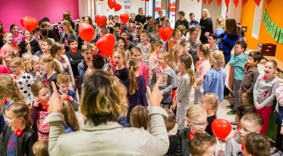 Decoratieve foto van basisschoolleerlingen. Samen met hun leraren zingen ze een lied. Ze houden ballonnen in de vorm van een hart vast.
