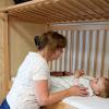 Decoratieve foto van een pedagogisch medewerker die een baby op bed legt